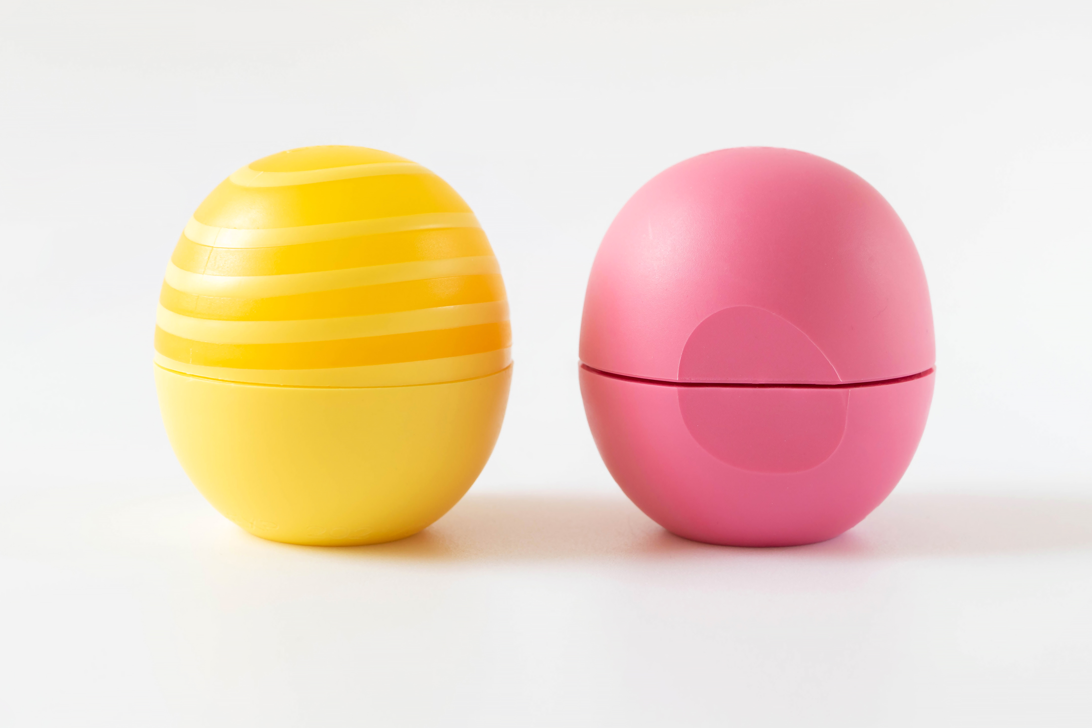 Two real round lip balm containers, one yellow and one pink, photographed on a white background