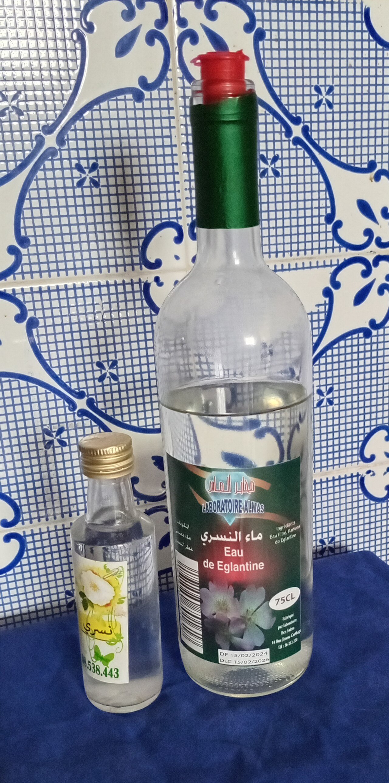 A clear bottle of dog-rose floral water beside fresh rose stems