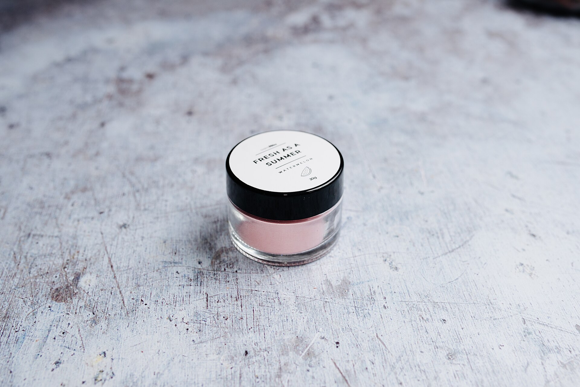 An open glass jar of pale pink cosmetic cream on a textured vanity surface
